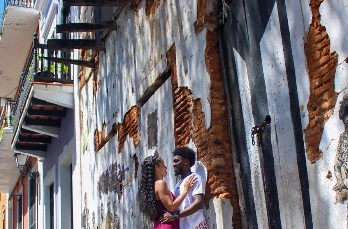 A couple stands close together in front of a brick wall adorned with artistic graffiti by the streets of San Juan.