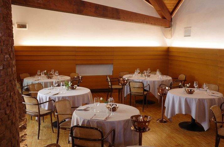 Due Spade restaurant's wooden interior theme with several round tables set with white tablecloths and chairs. 