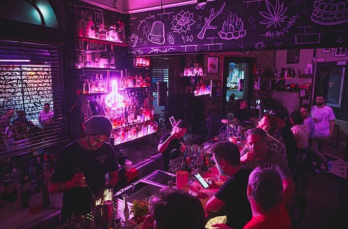 Bartenders serving drinks at the TRES MONOS BAR with pink neon signs and graffiti-decorated walls.
