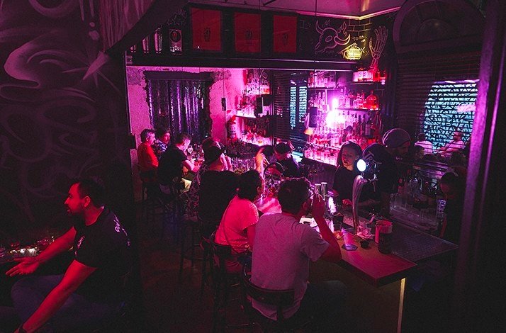 TRES MONOS BAR with guests seated at a neon-lit counter and dim red lighting.