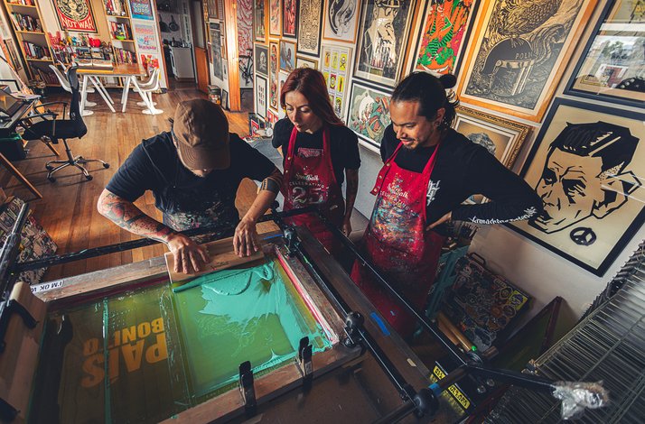 Artists collaborating on a screen-printing project in a studio filled with vibrant artworks on the walls