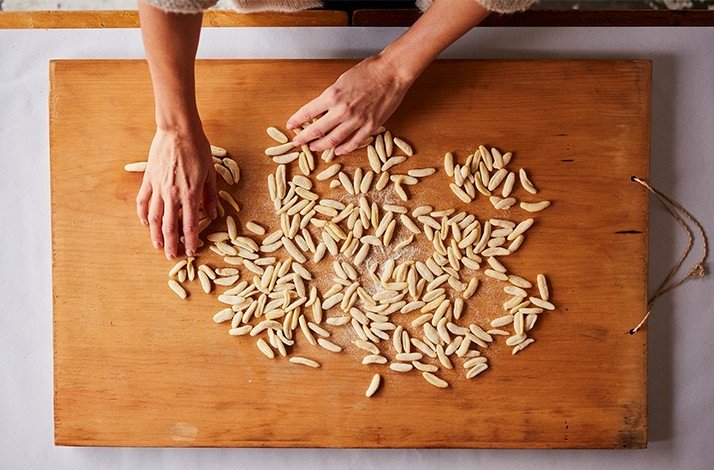 High-angle close-up view of a wooden cutting board with uncooked pasta arranged in a decorative pattern