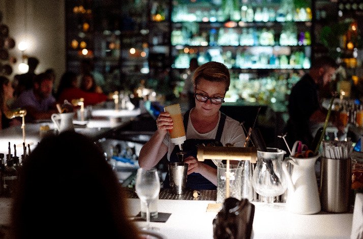 A lively bar scene, showcasing a bartender crafting a drink surrounded by bottles and glassware