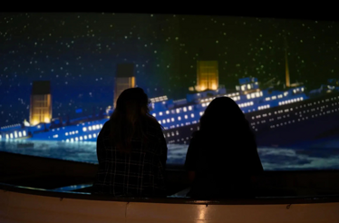 Two people with their backs to the camera exploring Titanic: An Immersive Voyage.