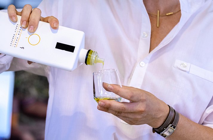 Man pouring olive oil from a white bottle into a tasting glass.