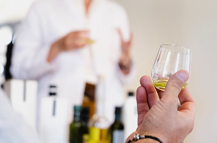 A glass containing olive oil with a person in a white lab coat on the background.