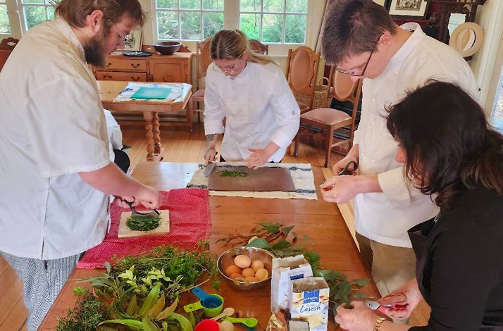 Several individuals in chef's attire are actively engaged in a cooking class, working together with various ingredients.