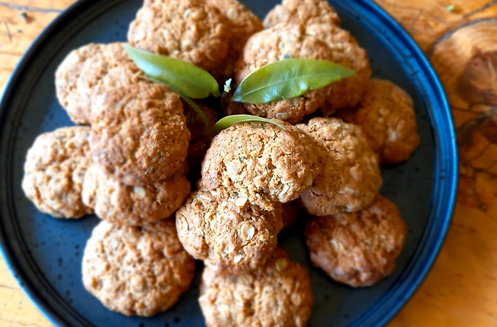 A dark-blue platter holds a pile of golden-brown oatmeal cookies, some topped with fresh green leaves.