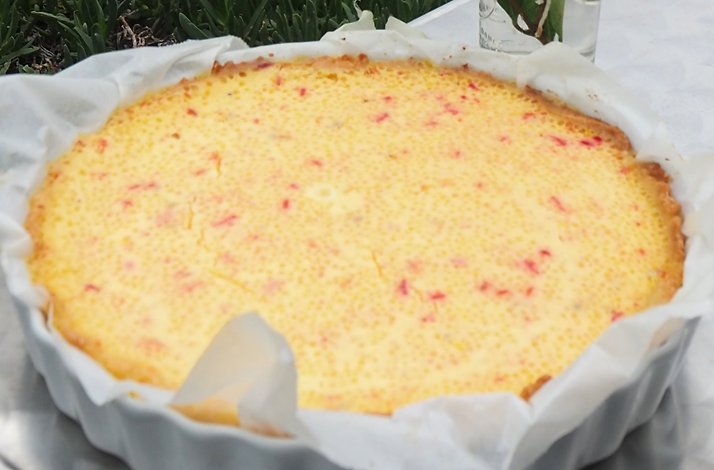 A round, light-yellow pie with small red specks is presented in a white baking dish lined with parchment paper.