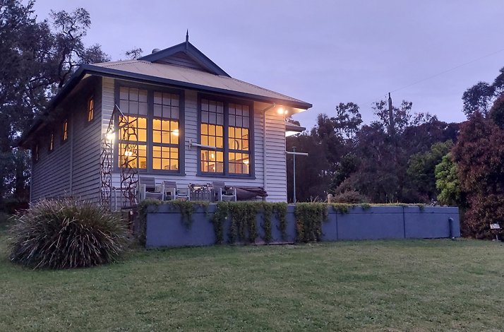 A small, light-colored house of the Peppermint Ridge Farm situated on a grassy hillside at dusk or dawn.