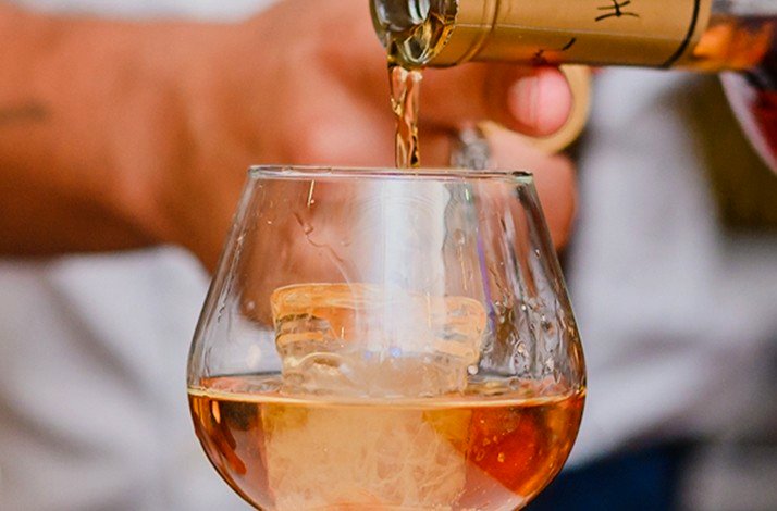A hand pours a premium golden drink into a glass over a large ice cube