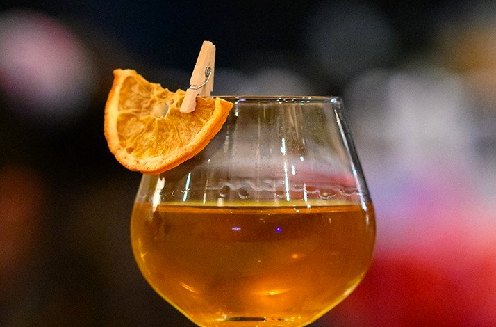A vibrant cocktail with a garnished orange slice clipped to the glass