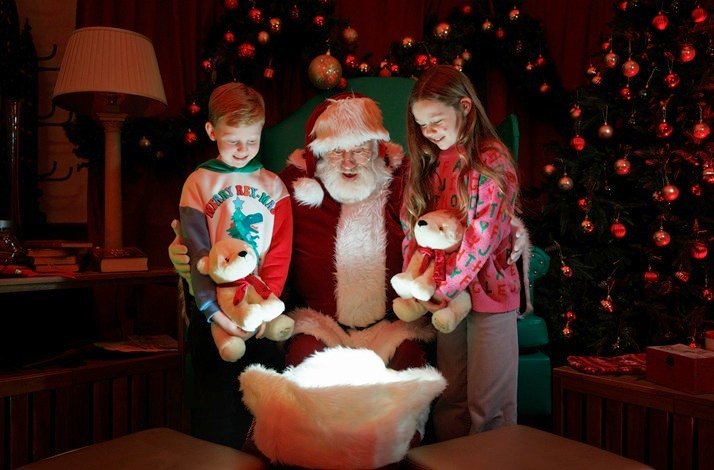 Three children are sitting with Santa Claus, appearing excited and happy.