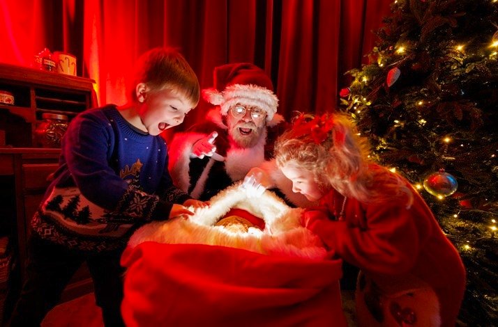 A group of children are excitedly looking into Santa's bag, which is lit up from the inside.
