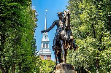 Statue of a mounted Paul Revere, a key figure in the American Revolution, on a tree-lined path.