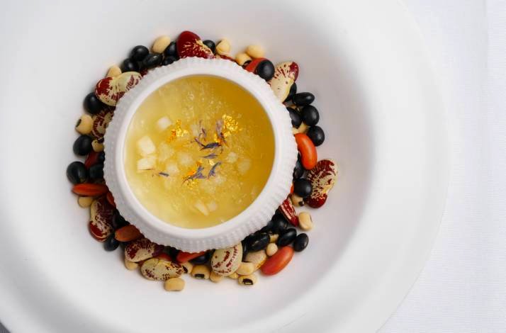 A creative dessert with a golden jelly served in a shell-shaped bowl, surrounded by colorful beans.