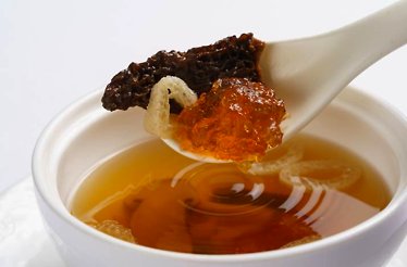 A close-up of mushroom, jelly, and noodles in spoon with the soup in bowl from YUAN Spring Tasting Menu on the background.