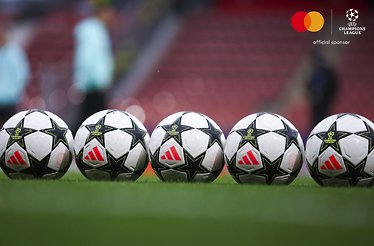 Five football balls with the UEFA Champions League logos on them lined on a football field