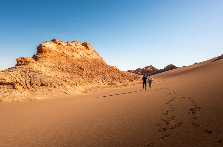 A couple walking and holding hands with their back to the camera in Salt Mountain Range, San Pedro de Atacama, Chile.