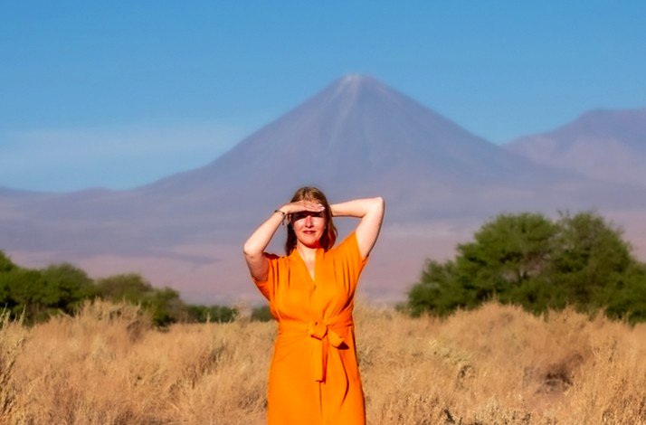 A woman dressed in orange covering her eyes from the sun for a photo in Salt Mountain Range, San Pedro de Atacama, Chile.