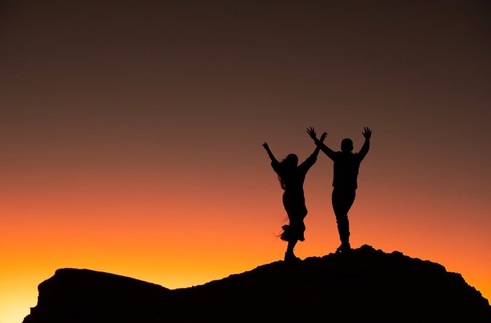 Silhouette of two people cheering at sundown.