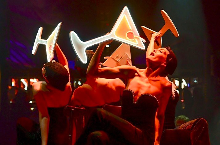Performers on the stage of Teatro Munich holding luminous cocktail signs.