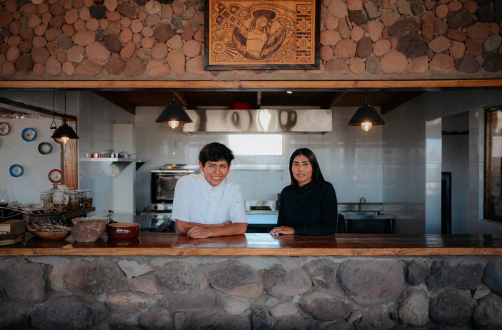 Rustic stone and wood kitchen counter with a chef and a serve, warm lighting and decorative artwork