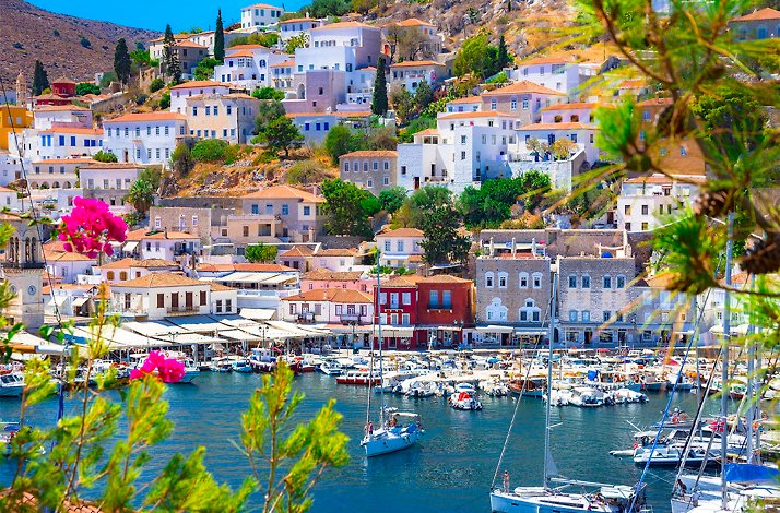 A picturesque view of a harbor in Hydra Island nestled on a hillside, with buildings lining the waterfront with some boats