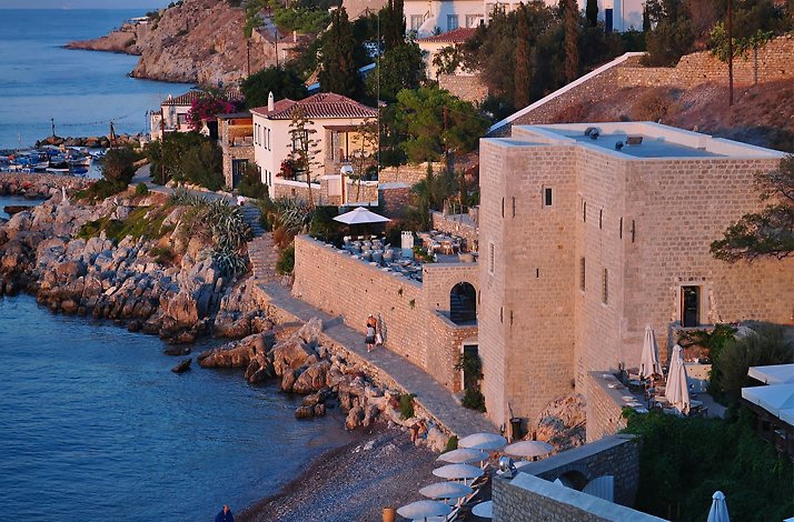 A picturesque coastal scene showcases a Mediterranean village at Hydra Island nestled along a rocky shoreline
