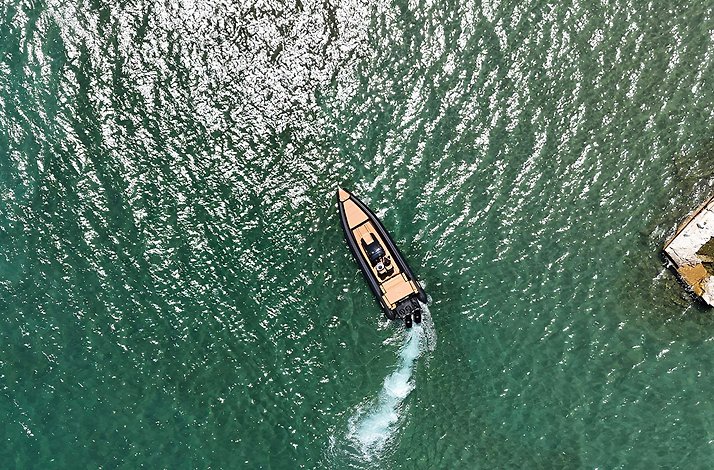 High-angle view of a black speedboat moving across teal-colored water
