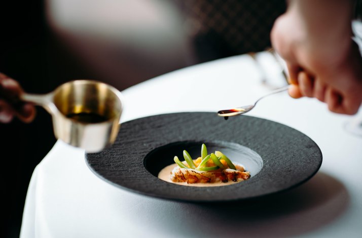 Special dish in a black plate with a souse being poured on.