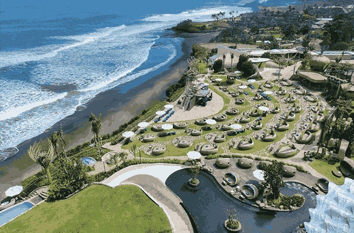Aerial view of Luna Beach Club with daybeds, pools, and oceanfront by a black sand beach.