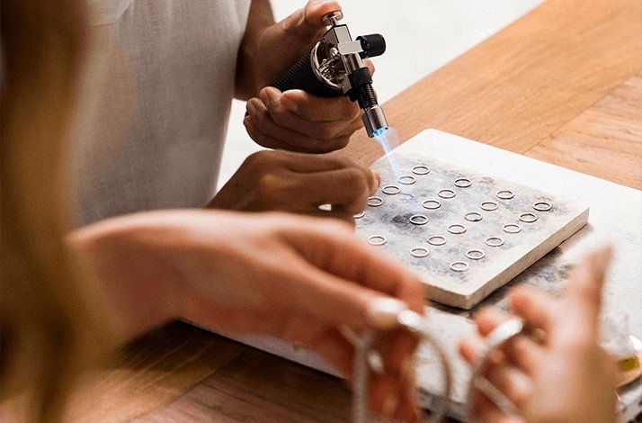 Hands using a torch to craft silver rings at John Hardy workshop in Bali.