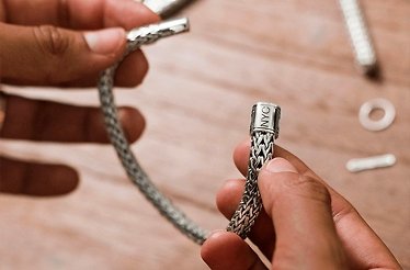 Hands holding a handcrafted silver bracelet at John Hardy workshop in Bali.