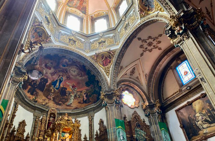 Interior of San Juan Bautista Church in Coyoacán, Mexico City, showcasing ornate domes, murals, and stained glass.