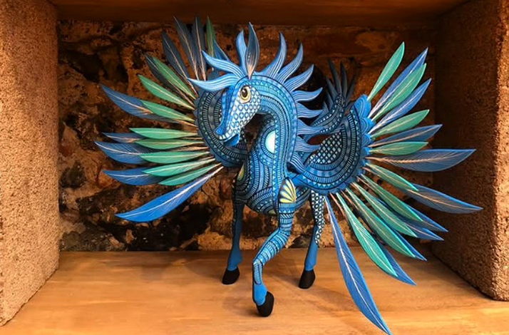An intricate blue and green statue of a mythical winged creature stands on a wooden shelf.