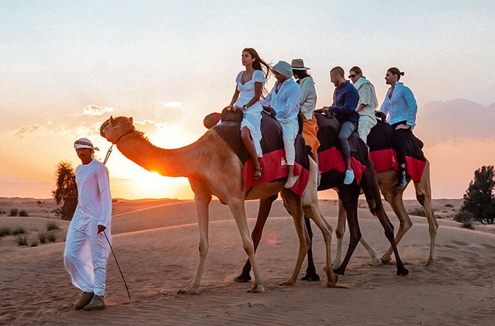 People riding camels at sunset in Dubai Desert Conservation Reserve.