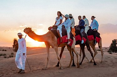 People riding camels at sunset in Dubai Desert Conservation Reserve.
