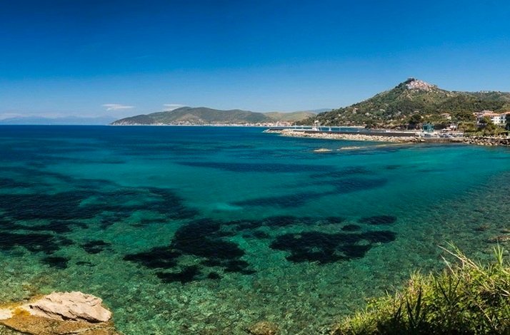 Clear turquoise sea with rocky seabed and a green hillside under a bright blue sky