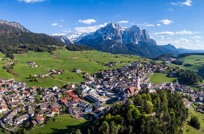Aerial view of an alpine village with green fields and mountains in the background