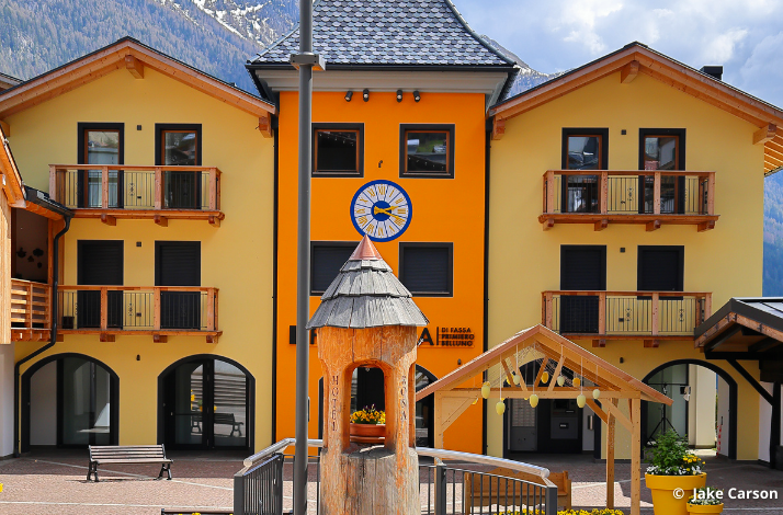 Yellow-orange alpine building with balconies and a clock.