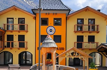 Yellow-orange alpine building with balconies and a clock.