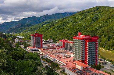 Călimănești-Căciulata Spa Resort with red buildings, green hills, and Olt River.
