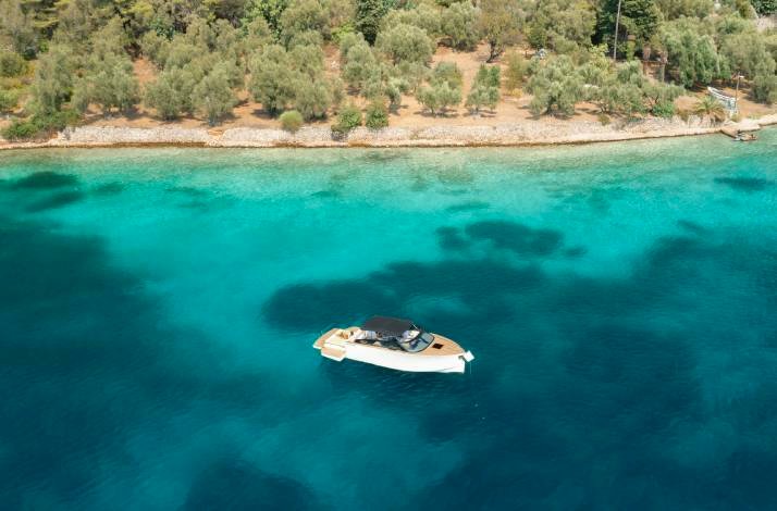 High-angle view of a white motorboat on calm, clear turquoise water, surrounded by a shoreline with trees at Dubrovnik. 