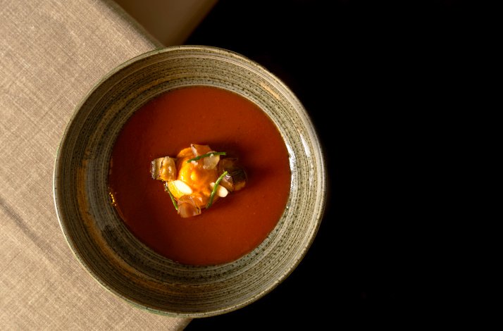 A beautifully presented bowl of rich red soup garnished with fresh, vibrant ingredients