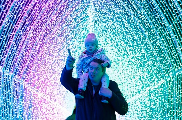 A man carrying a child on his shoulders inside a bright light tunnel at Wonderlights in Malahide Castle.