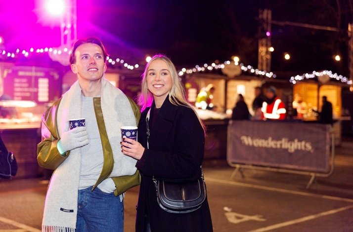 A smiling couple holding warm drinks at the Wonderlights festival village in Marlay Park.