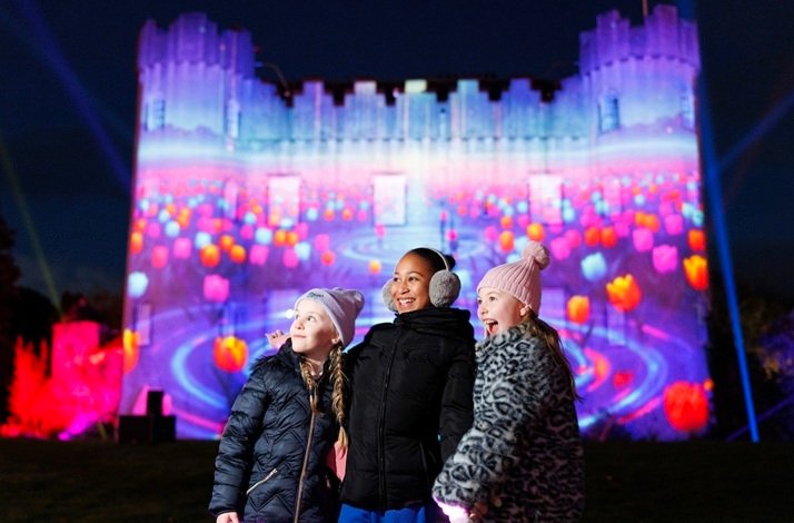 Three girls smiling in front of Malahide Castle during the Wonderlights light show.