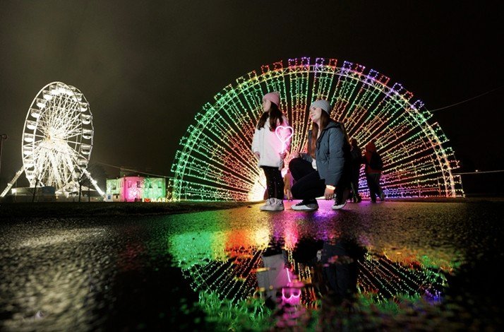 Children in front of giant wheels lit with colorful lights at night.