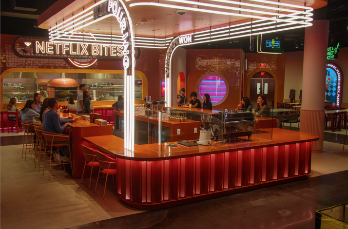 Interior of Netflix Bites restaurant featuring a vibrant orange bar lit with neon 